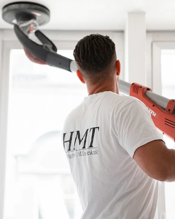 En målare från Herrängens Måleriteknik slipar ett tak med maskin. Vi levererar måleri med högsta kvalitet och precision vid nyproduktion.